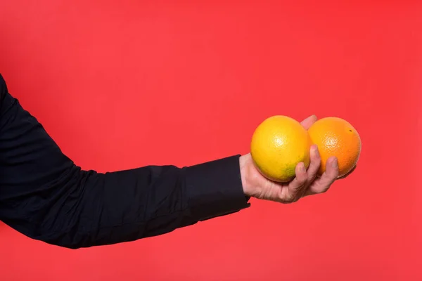 Mão Segurando Duas Frutas Laranja Fundo Vermelho — Fotografia de Stock