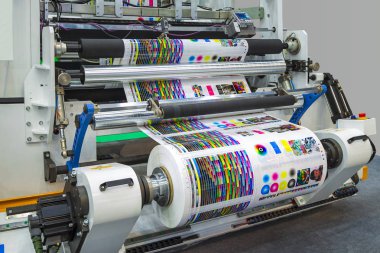 Büyük ofset matbaa veya dergi endüstriyel yazıcı makinesinin üretim hattında uzun bir rulo kağıt çalıştırıyor.