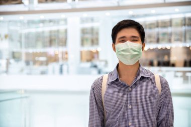 Yeni normal yaşam tarzında tıbbi koruyucu maskenin ardında gülümseyen Asyalı bir adam..