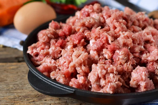 Carne crua em uma frigideira de ferro fundido em um fundo de madeira — Fotografia de Stock