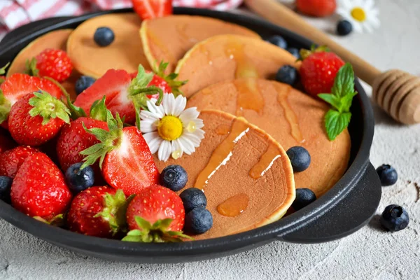 Pancakes with berries and honey in a pan on a concrete backgroun — Stock Photo, Image