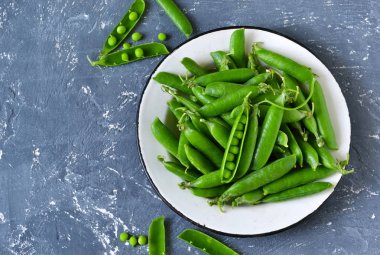 Bir beton zemin üzerine bir tabak taze, genç yeşil bezelye. 