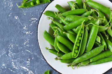 Bir beton zemin üzerine bir tabak taze, genç yeşil bezelye. 