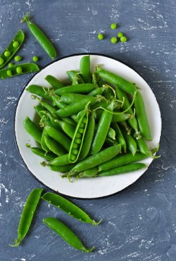 Bir beton zemin üzerine bir tabak taze, genç yeşil bezelye. 