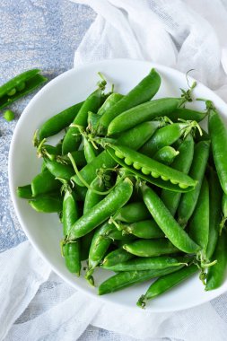 Bir beton zemin üzerine bir tabak taze, genç yeşil bezelye. 