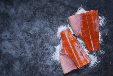 Salmon fillet with spices and salt on a black stone background.