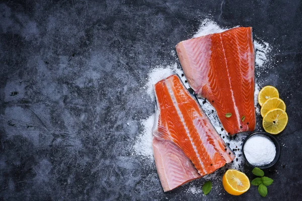 Salmon fillet with spices and salt on a black stone background.