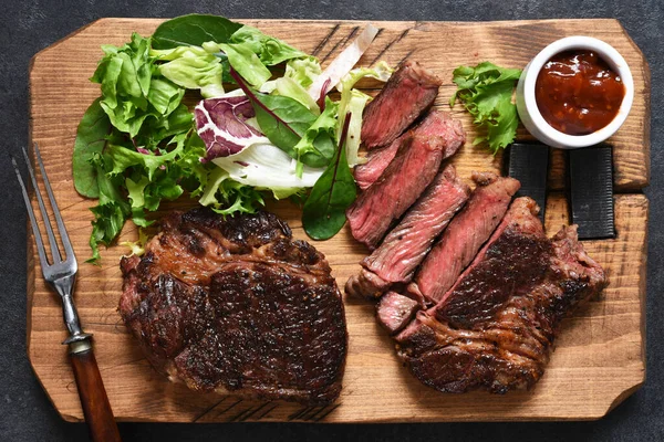 Bistecca di manzo alla griglia con insalata su una tavola di legno — Foto Stock