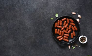 Siyah zemin üzerinde dökme demir bir tavada baharatlı sucuk ve metin için yer var..