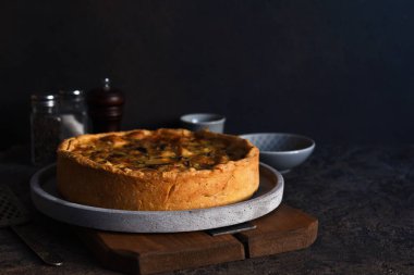 Koyu beton arka planda tavuk, mantar ve peynirli kiş. Mutfak masasının üstünde..