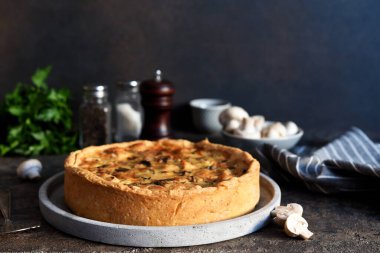 Koyu beton arka planda tavuk, mantar ve peynirli kiş. Mutfak masasının üstünde..