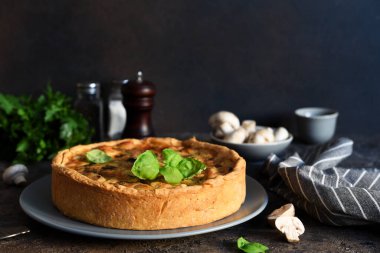 Koyu beton arka planda tavuk, mantar ve peynirli kiş. Mutfak masasının üstünde..