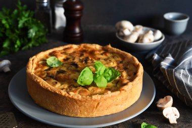 Koyu beton arka planda tavuk, mantar ve peynirli kiş. Mutfak masasının üstünde..