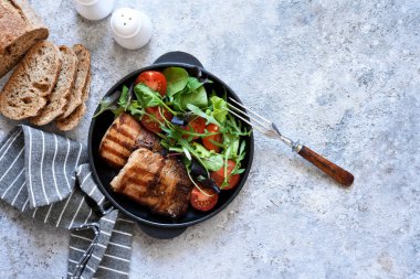 Beton arka planda tavada karışık salata ve sebzeli ızgara biftek..