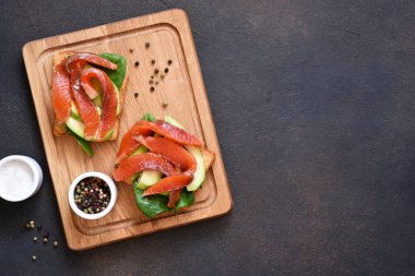 Beton bir arka planda tahtada avokado ve somonlu tost..