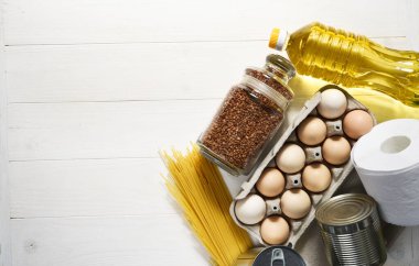 Beyaz ahşap arka planda gıda bağışları: yağ, karabuğday, yumurta, konserve yiyecek. Evinde otur. Karantinaya alın. Yemek teslimatı.