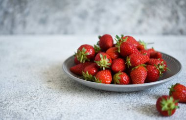 Beton arka planda bir tabakta taze çilek ve metin için yer var. Yatay odak.