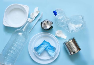 Mavi arka planda plastik çöp: tabaklar, şişeler, polietilen, maske. Çevre kirliliği. Ekolojik felaket.