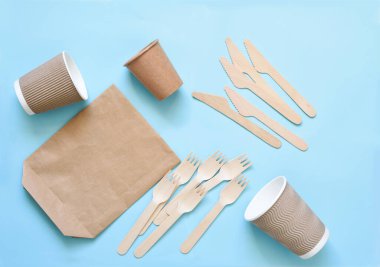 Tek kullanımlık eko-kağıt tabaklar: cam, karton, çanta, çatal, bıçak. Boş mavi bir arkaplanda. Mavi arka plandaki ahşap çatal bıçak düzeni..
