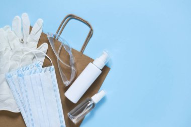 Virüs koruması: antiseptik, maske, eldiven, mavi arka planda gözlük. Satın alınabilen kağıt poşet. Düz. Salgın..