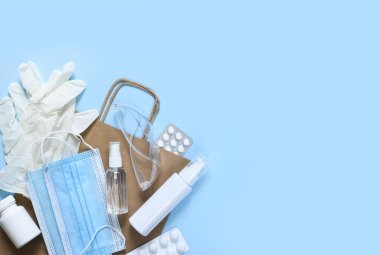 Antivirüs aksesuarları: antiseptik, maske, mavi arka planda eldivenler ve haplar. Kraft kağıt paketi..