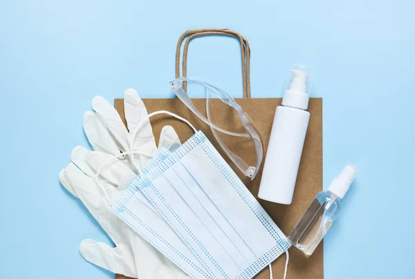 Virus protection: antiseptic, mask, gloves, glasses on blue background. Craft paper bag with purchase.Flatly.Pandemic.