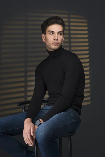 Стильный молодой человек в черном свитере сидит рядом с жалюзи и thinki — стоковое фото