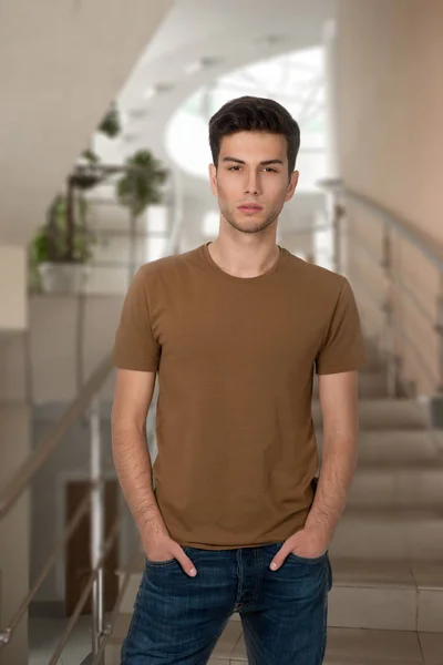 O rapaz jovem em uma camisa e jeans olha na câmera — Fotografia de Stock