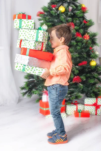 O rapaz mantém na mão muitos presentes em um abeto de Cristmas — Fotografia de Stock