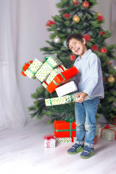 男孩手里拿着许多礼物在一棵圣诞冷杉树 — 图库照片