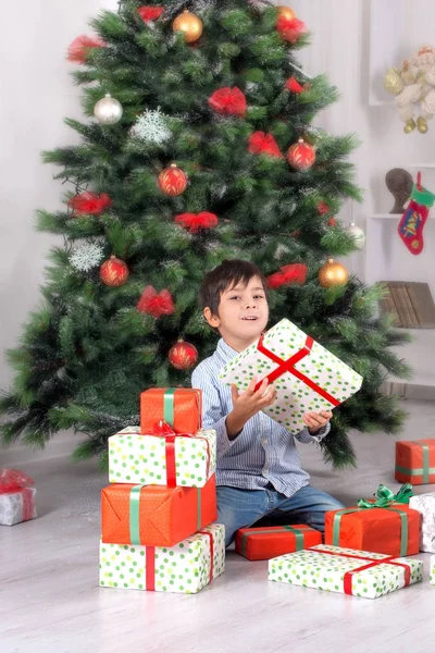 O rapaz mantém na mão muitos presentes em um abeto de Cristmas — Fotografia de Stock