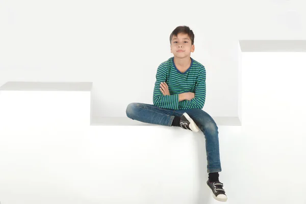 Der Junge sitzt auf weißen Stufen oder Kisten im Studio — Stockfoto