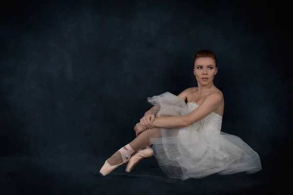 A bailarina em pointes e um vestido branco senta-se — Fotografia de Stock