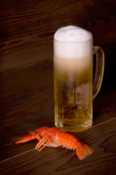 Vidro com cerveja e um lagostim fervido estão em uma mesa de madeira — Fotografia de Stock