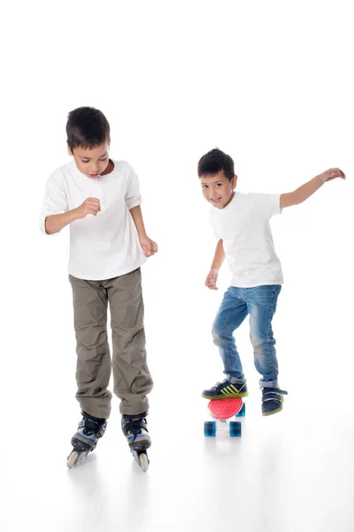 Два мальчика катаются на роликовых коньках и доске на белом фоне в студии — стоковое фото