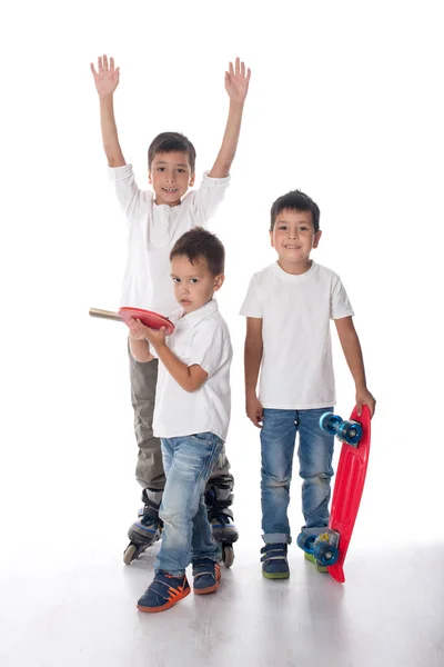 Три хлопчики в роликових ковзанах, з дошкою і з ракеткою — стокове фото