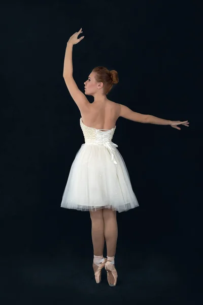 A bailarina em pointes e um vestido branco dança em umas costas escuras — Fotografia de Stock