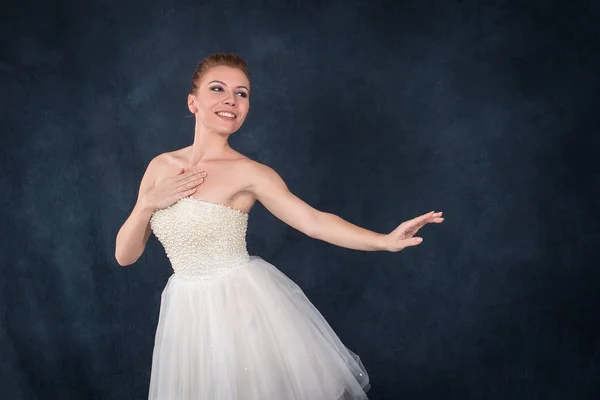 A bailarina em pointes e um vestido branco dança em umas costas escuras — Fotografia de Stock