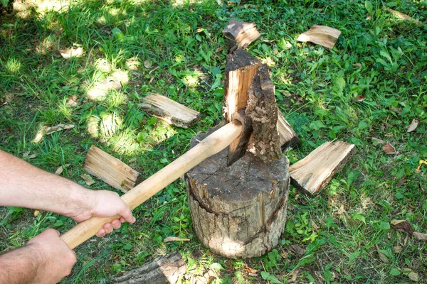 Pria itu memotong kayu bakar dengan kapak di rumput hijau . — Stok Foto