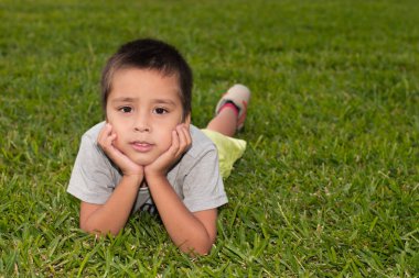 Çocuk bir yüz eller yukarı yaslanır yeşil çimenlerin üzerinde yatıyor