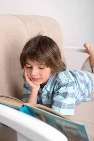 Den lilla pojken i en blå t-shirt på en soffa med bok — Stockfoto