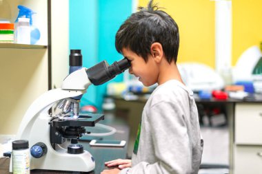 Okullu çocuk bir laboratuvarda mikroskopa bakıyor.