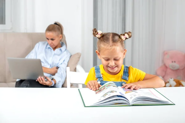 Знімок усміхненої дівчини, що сидить за столом вдома і читає б — стокове фото