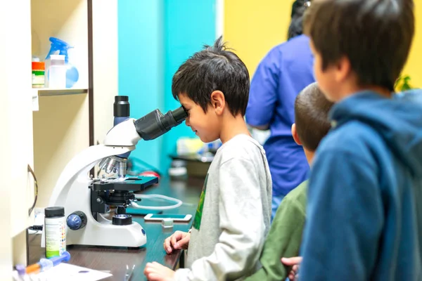 The schoolboy looks through a microscope in a laboratory with cu — Stock Photo, Image