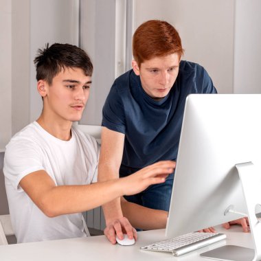 İki ciddi genç adam bilgisayar kullanıyor ve bir şeyler tartışıyorlar.