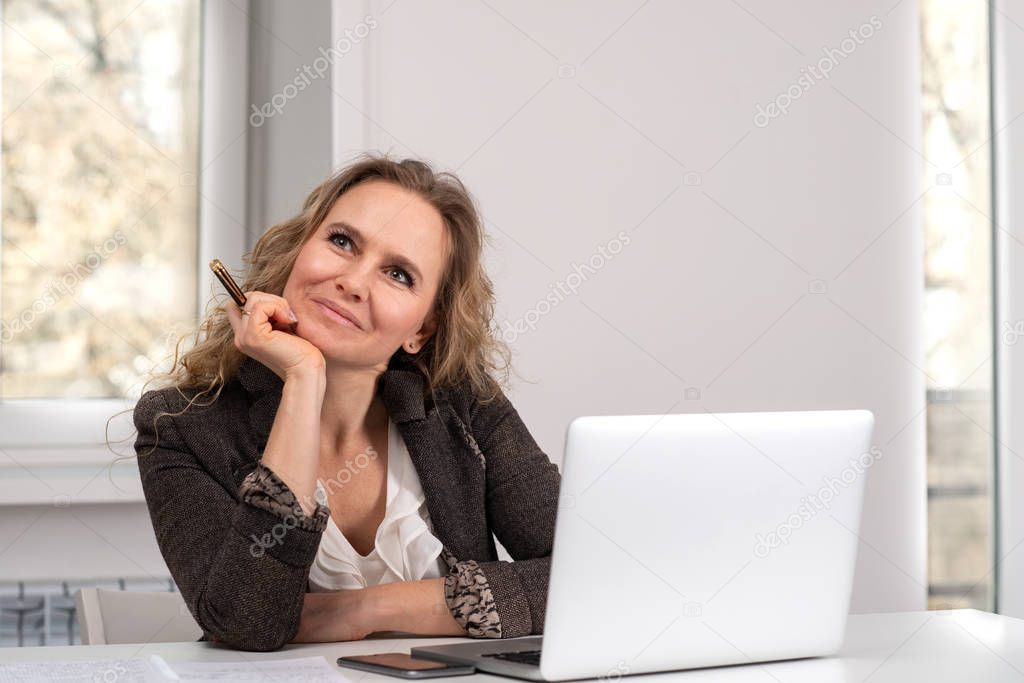 A young woman   works on  laptop and dreamily looks to the side