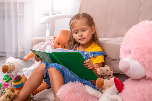 Знімок маленької дівчинки, що читає книгу зі своїм плюшевим ведмедем та іншими — стокове фото