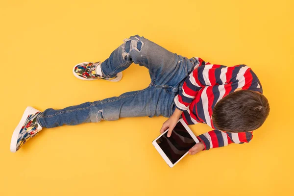 Colegial niño se sienta en un fondo amarillo y navega por el interno — Foto de Stock