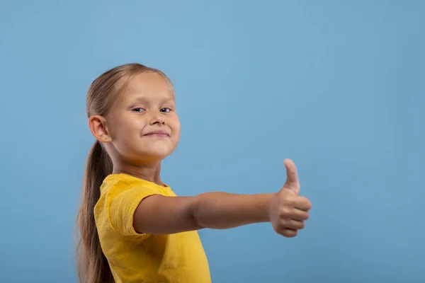 Молода усміхнена дівчина дає тобі схвальний жест проти блакитного — стокове фото