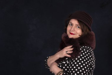 Kürk pelerinli ve şapkalı yaşlı bir kadının yarım boy portresi. Fotokopi alanı olan koyu bir arka plana flört ediyor.